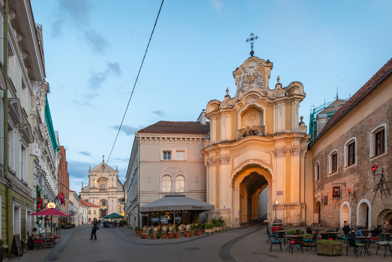 a stone street lined with building fronts and a church and one person walking